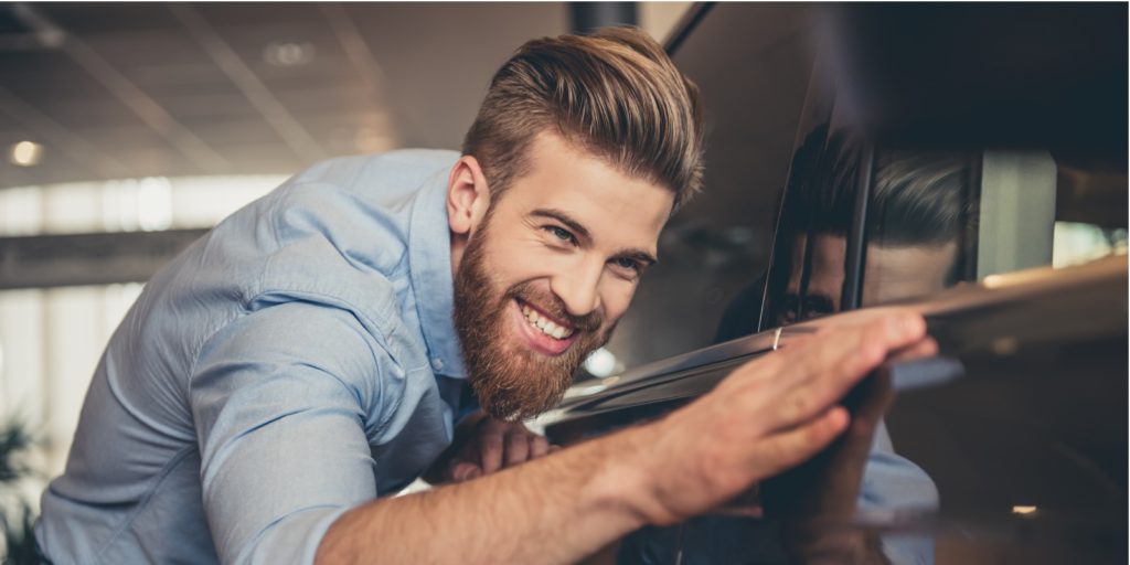 A bearded man is stroking his just bought classic car.