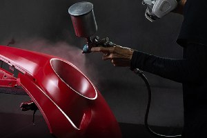 A custom auto body mechanic applying red paint on a bumper