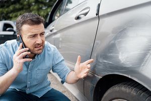 man on phone looking at dent in car